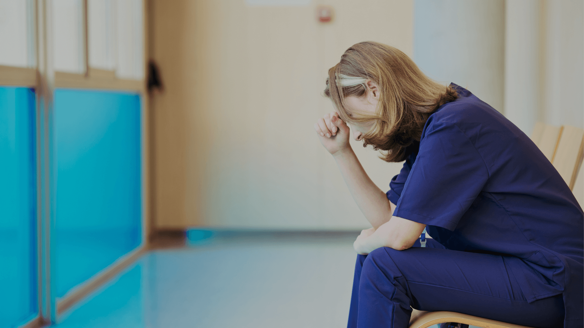 Gefrustreerde zorgmedewerker voorovergebogen in ziekenhuisgang