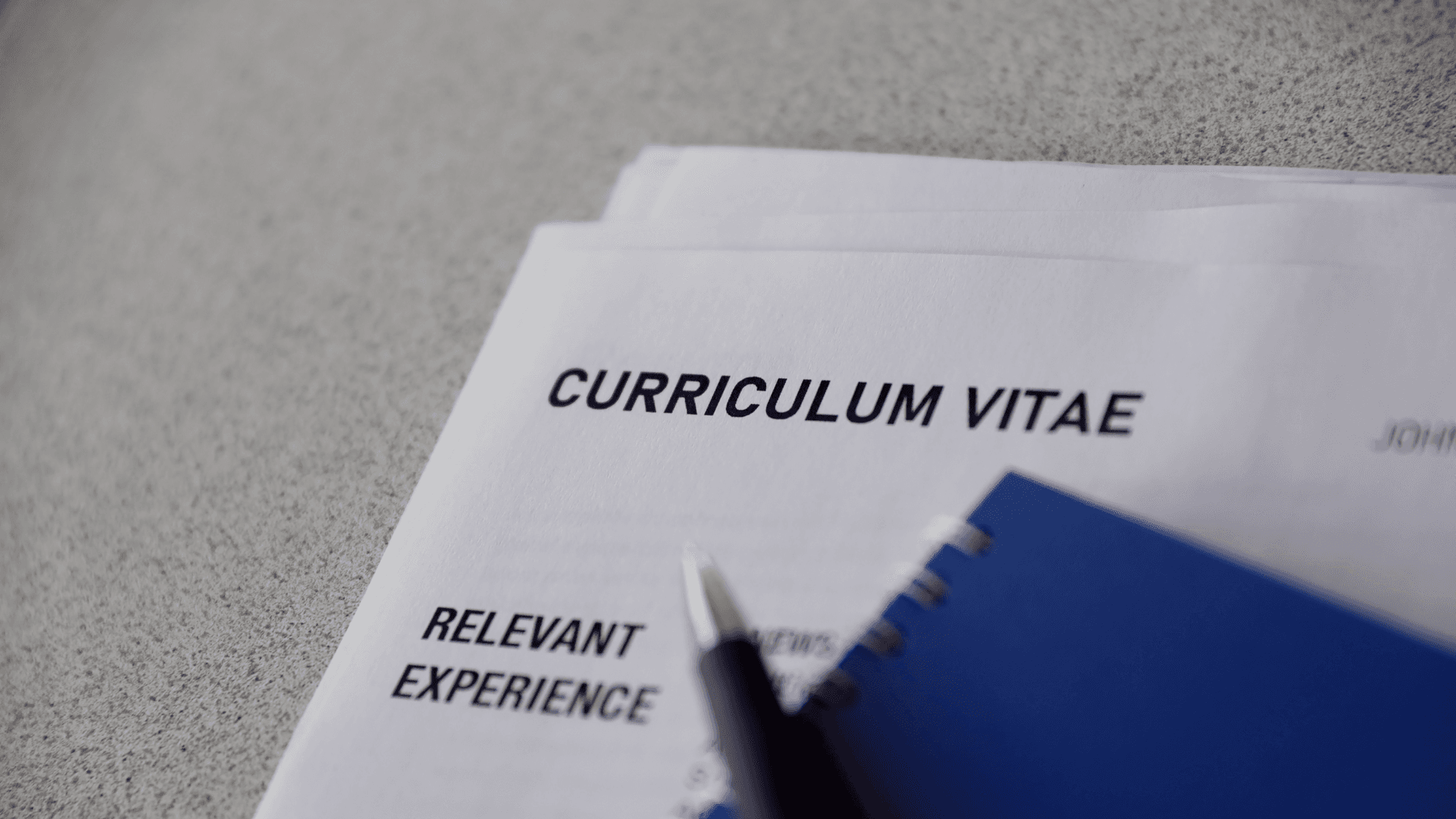 Close-up van een cv-document met een pen en een blauw notitieboek op een grijs oppervlak