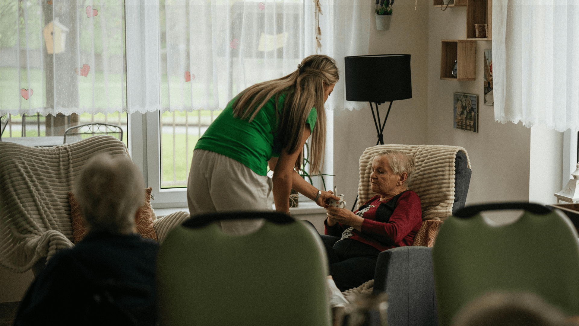 Huishoudelijke hulp geeft kopje thee aan bewoner in woonkamer
