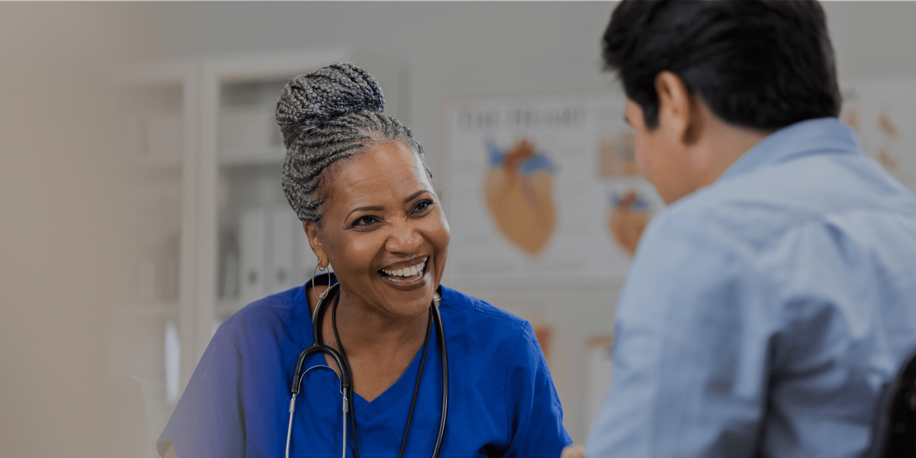Zorgmedewerker met stethoscoop in gesprek met patiënt in behandelruimte